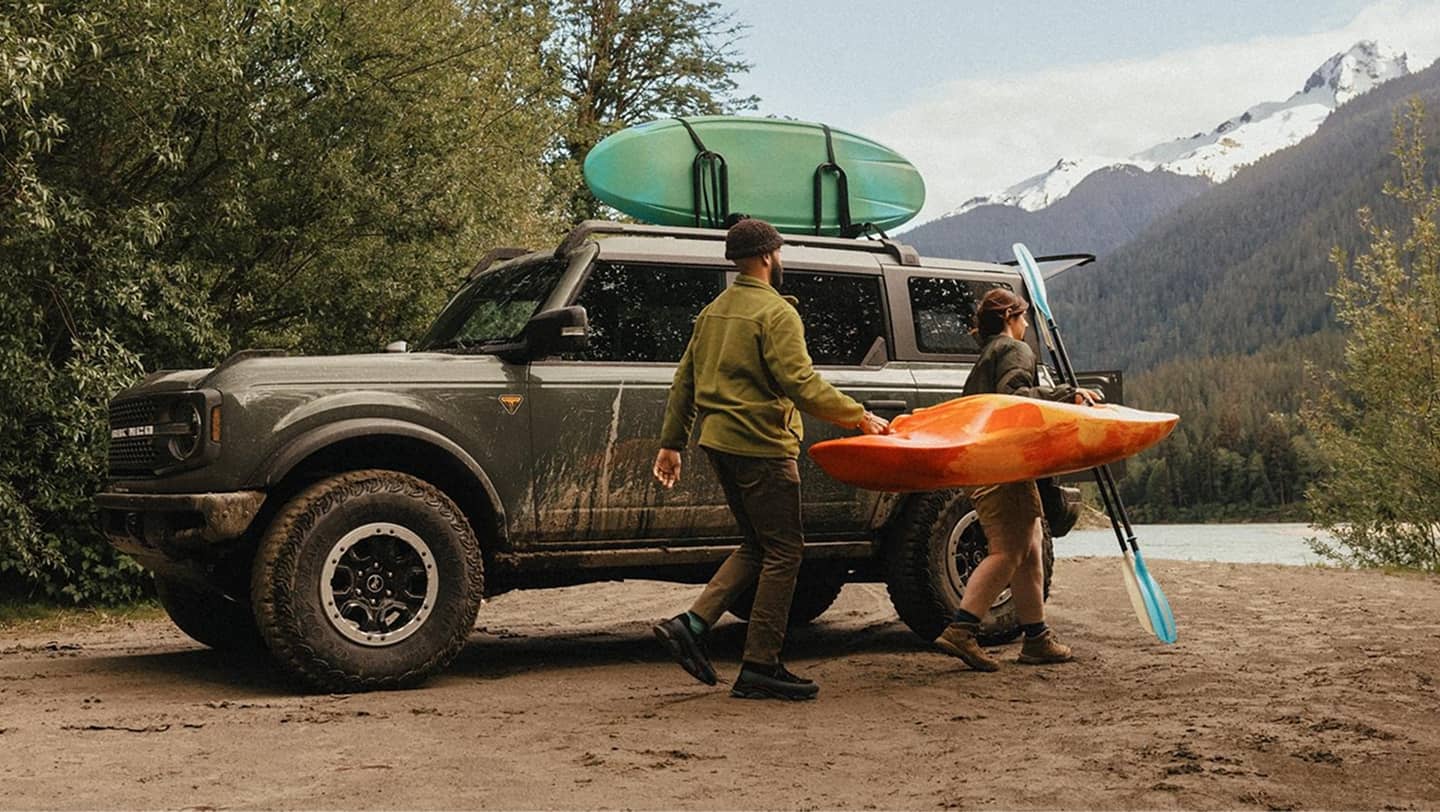 People walking next to 2026 bronco by mountains and trees