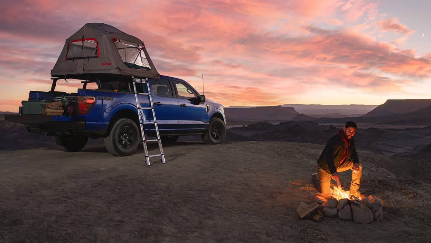 man starting fire next to ford f-150 with tent on top outside