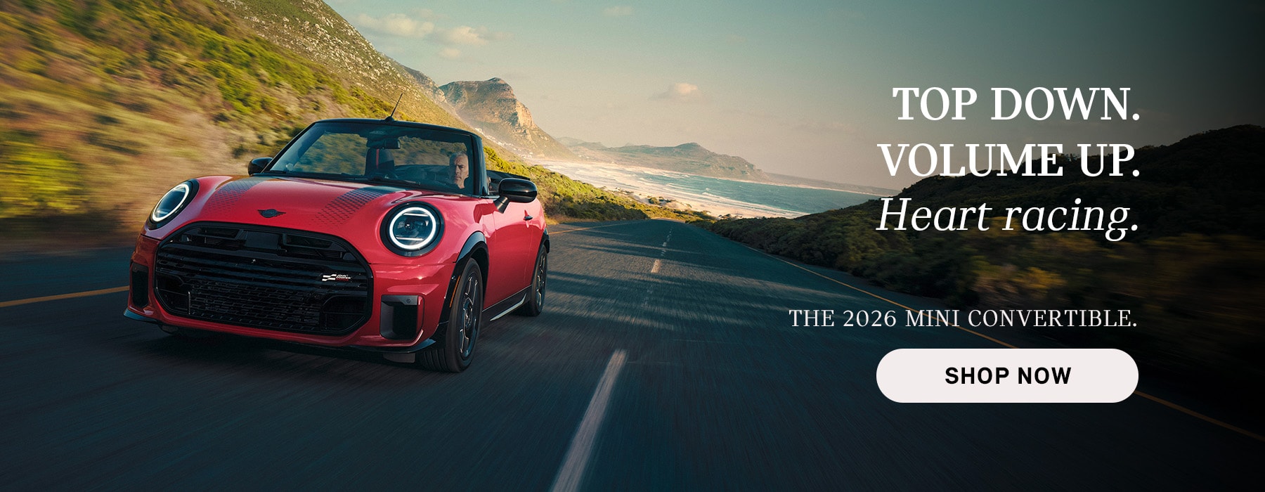 Red MINI convertible driving along a coastal road with mountains and ocean in the background, with advertisement text promoting the 2026 Mini Convertible and a “Shop Now” button.